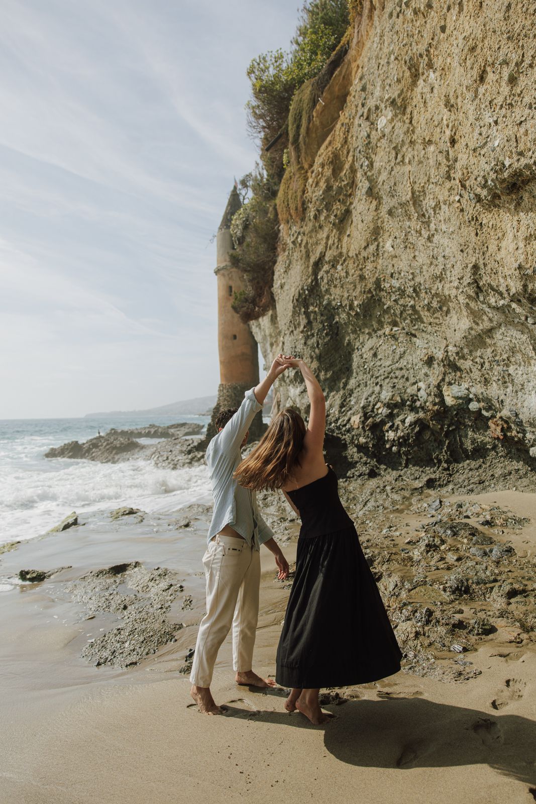 McKenna and Chandler dancing barefoot on the beach beneath a cliff